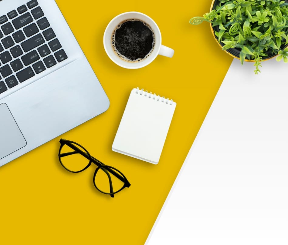 A desk area with a laptop, glasses, pad of paper, and coffee cup